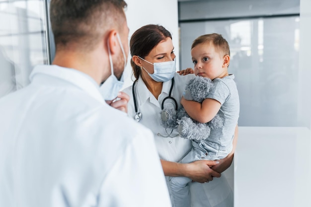 With little boy that being examined Two doctors in white coats is in the clinic working together