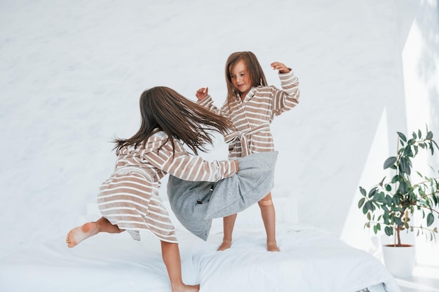 With pillows in hands Two cute little girls indoors at home together Children having fun