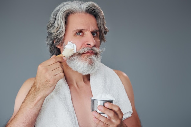 With shaving gel Stylish modern senior man with gray hair and beard is indoors