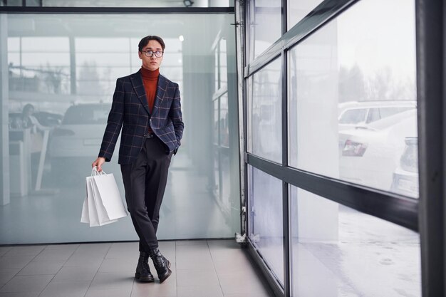 With shopping bags. Young business man in luxury suit and formal clothes is indoors in the office.