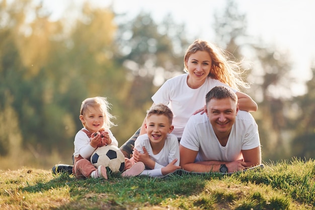 With soccer ball Happy family lying down outdoors near the forest With daughter and son