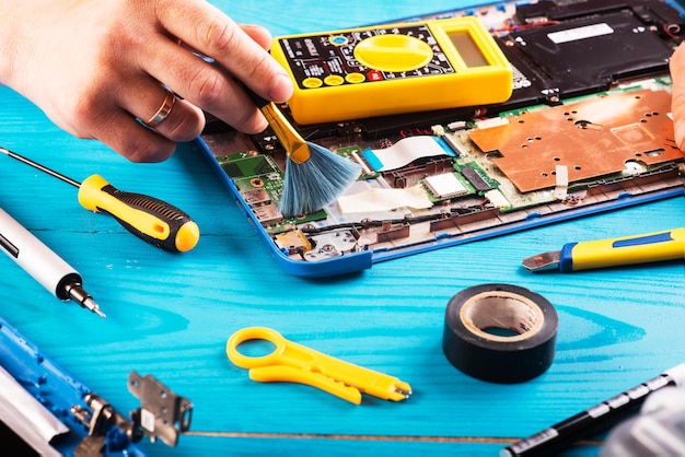 Wizard repairs laptop with tools and hands on the blue wooding table top view