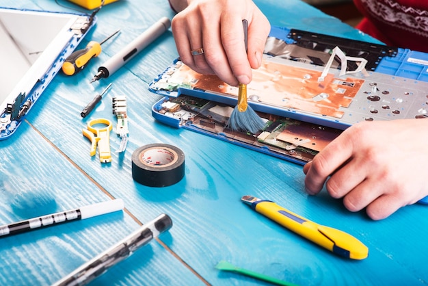 Wizard repairs laptop with tools and hands on the blue wooding table top view