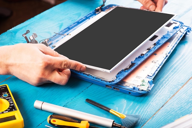 Wizard repairs laptop with tools and hands on the blue wooding table top view