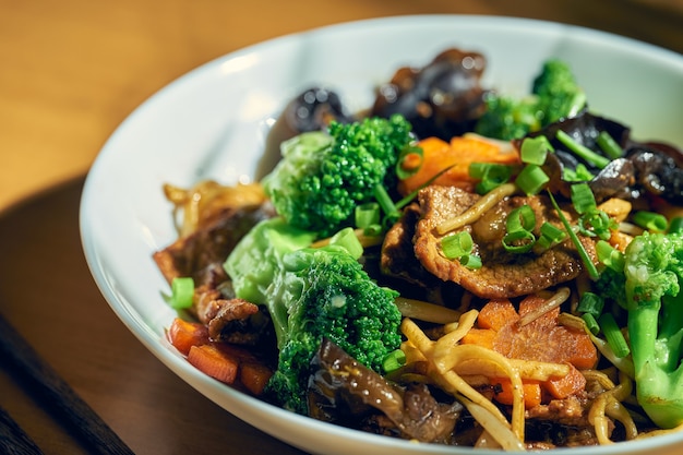 Wok noodles with beef, vegetables, sweet and sour sauce and Sichuan pepper. Wood background. Chinese cuisine