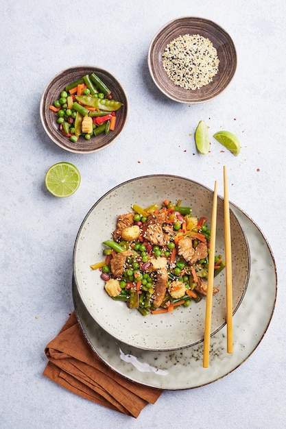 Wok with turkey meat corn green peas green beans and carrots served on gray background with chopstic