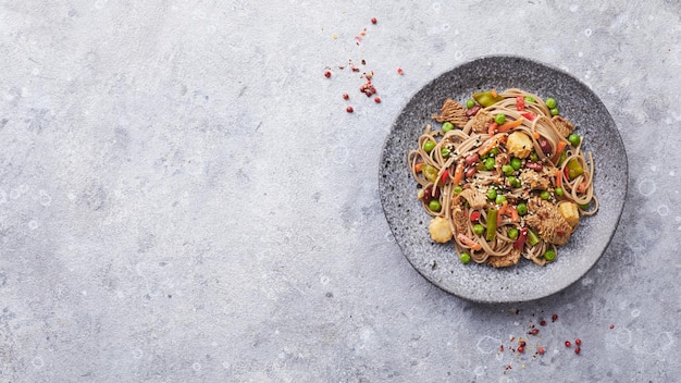 Wok with turkey meat soba noodles corn green peas green beans and carrots served on gray background