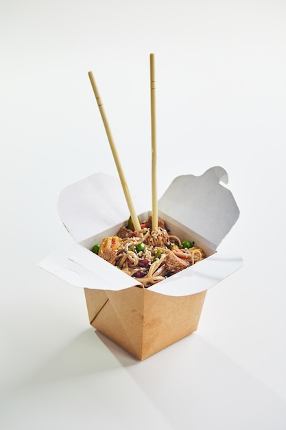 Wok with turkey meat soba noodles paprika mushrooms and carrot in takeout box with chopsticks