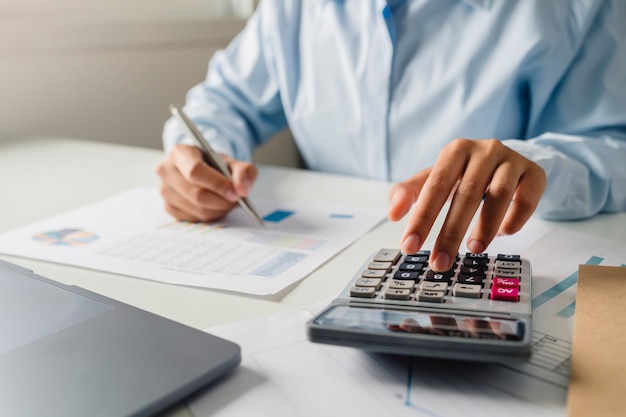 Woman accountant use calculator and computer with holding pen on desk in office. finance and accounting concept