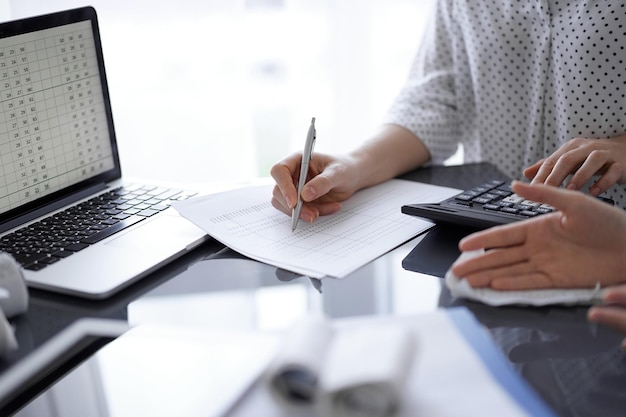 Woman accountant using a calculator and laptop computer while counting and discussing taxes with a client. Business audit concepts