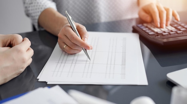 Woman accountant using a calculator and laptop computer while counting taxes for a client. Business audit and finance concepts