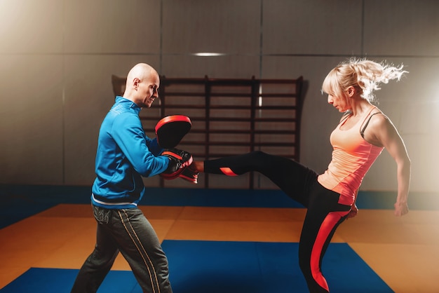 Woman in actoin on self defense workout with personal instructor, fighting training in gym, martial art