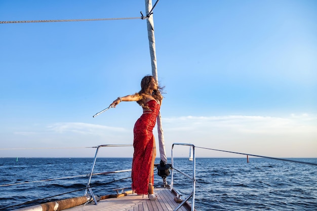 Woman actress in red stage costume with flute posing on yacht at sea and blue sky background Female in theatre clothes outdoors