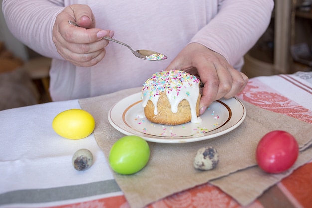 Woman adding sprinkles on the top of the Easter cake. Colored eggs on a table