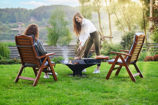 Woman adds pepper to a steak on the grill and her friend is watching