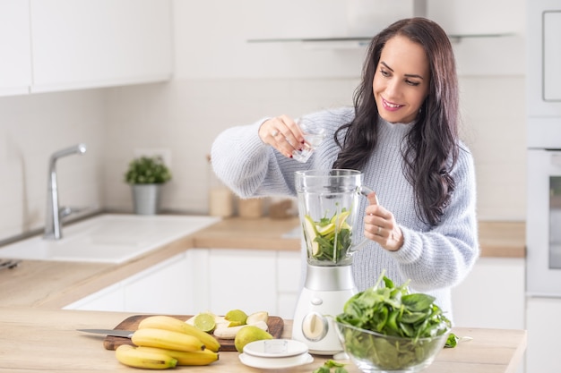 Woman adds water into a mixer for a spinach, banana, and apple smoothie.