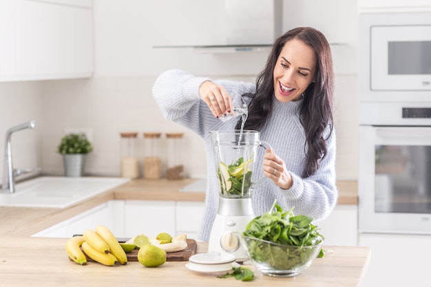 Woman adds water into a mixer for a spinach, banana, and apple smoothie.