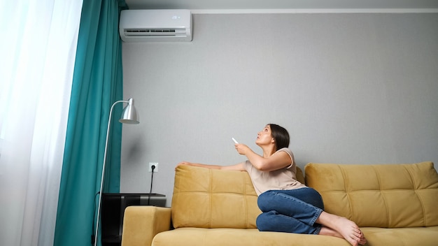 Woman adjusts the air conditioner while sitting on the couch.