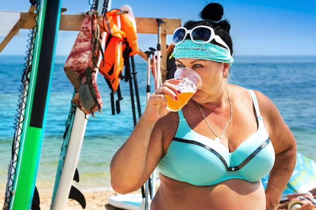 A woman aged drinks beer on the beach