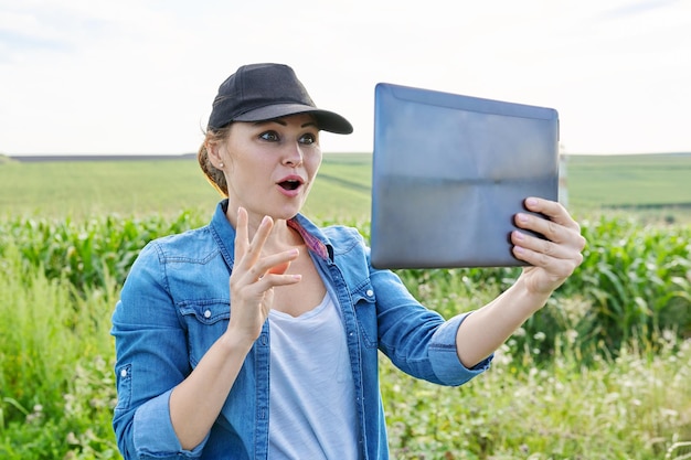 Woman agricultural worker inspecting corn field video call using digital tablet