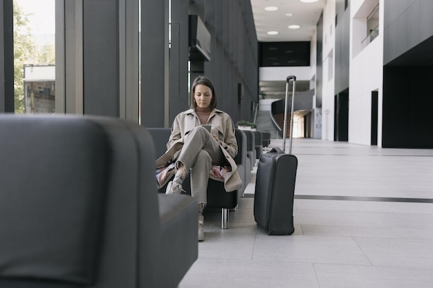 Woman at the airport or congress center with a suitcase is sitting in the waiting area and chatting