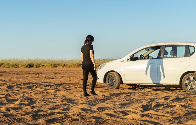 Woman alone dressed in dark clothes approaching a white car at the sunrise