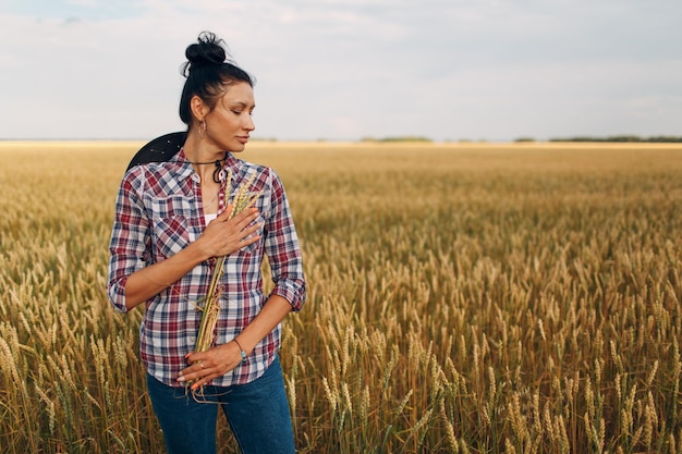 Woman american farmer with sheaf ears wearing cowboy hat plaid shirt and jeans at wheat field