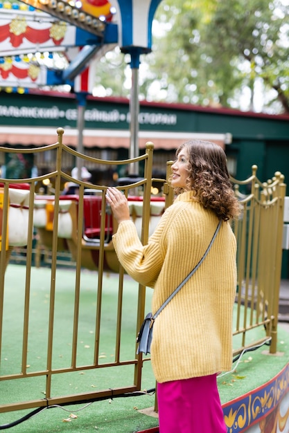 Woman in an amusement park look on a carousel and smiles with happiness the concept of weekends