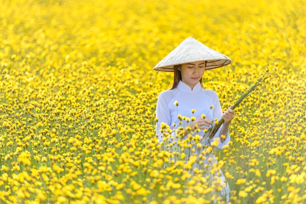 A woman in an ancient Vietnamese national costume Was standing holding a hat made of wickerwork among the yellow flowers