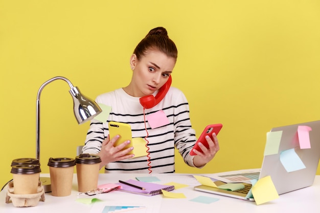 Woman answering call on landline at workplace all covered with sticky notes holding mobile phones