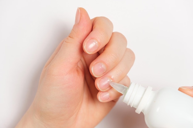 Woman applies cuticle remover to nails on white background