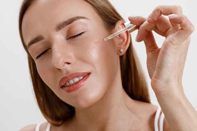 Photo woman applies on her face cosmetics moisturizing serum or oil facial essence on studio background