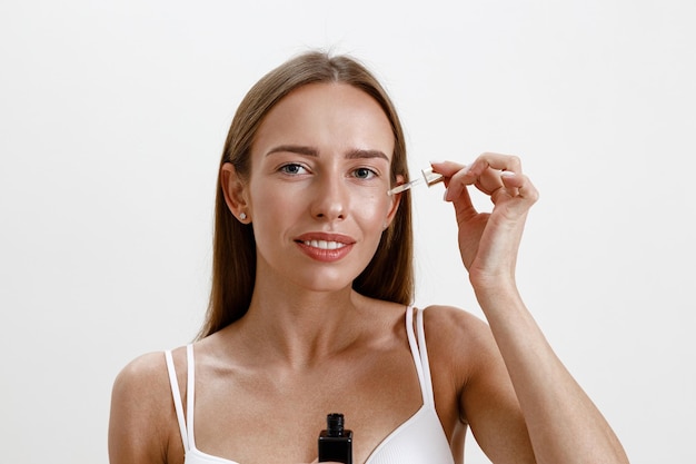 Photo woman applies on her face cosmetics moisturizing serum or oil facial essence on studio background