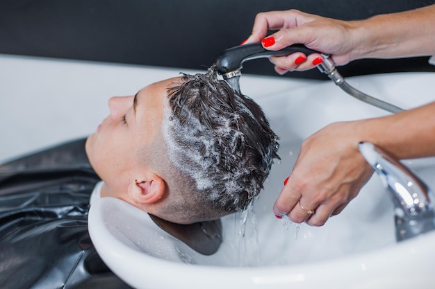 A woman applies shampoo and massages a client's hair The guy is washing his hair at the barbershop