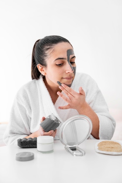 Woman applying clay face mask at home