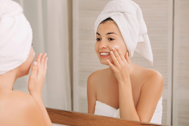 Woman applying cream on her face in bathroom