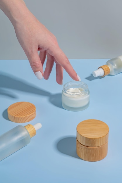 Woman applying cream on her hand on blue background with cosmetic products and hard shadows Skin care treatment concept