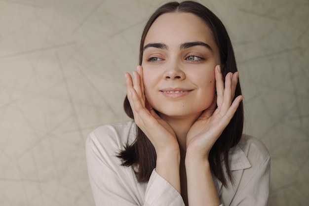 woman applying face cream gently and doing skincare beauty routine while looking away at home