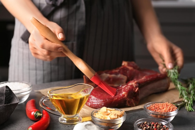 Photo woman applying oil onto raw steak with silicone brush in kitchen