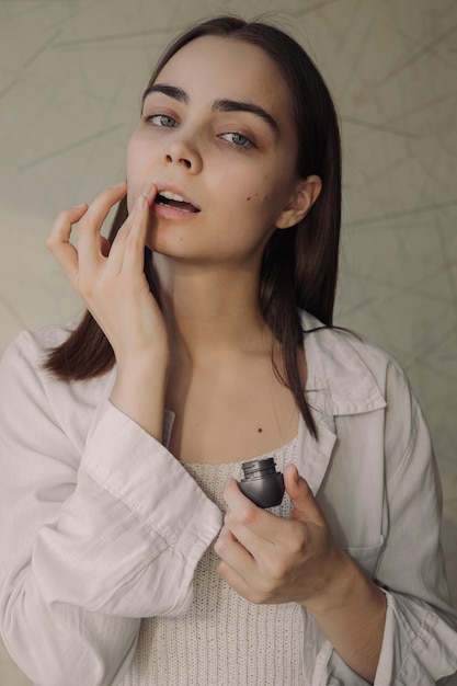 woman applying protective lip balm with finger while doing skin care beauty routine