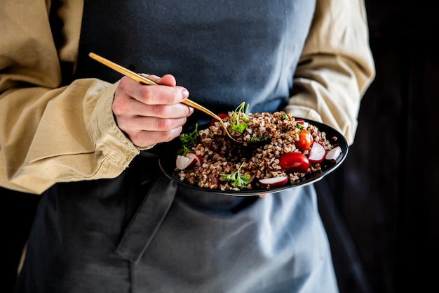 Woman in an apron holds a plate of buckwheat in her hands