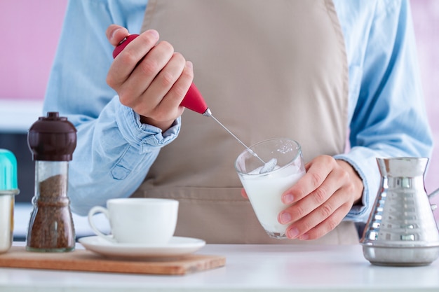 Woman in apron using a milk frother for making coffee at kitchen at home