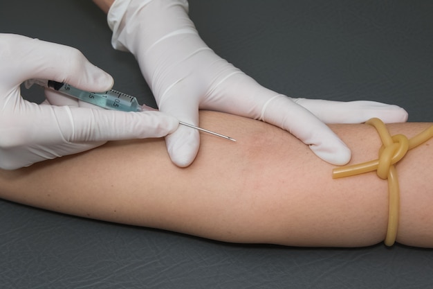 woman arm with a tourniquet getting injection with a syringe at hospital