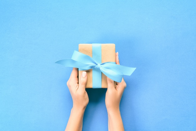 Woman arms holding gift box with blue ribbon on blue