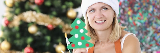 Photo woman artist in santa hat holding toy christmas tree and paint brushes choosing picture as gift