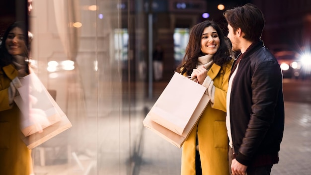 Woman asking boyfriend to buy clothes standing near shop window