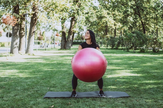 Woman athlete with a big fitness ball trains in the park