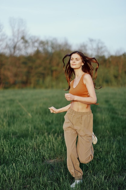 A woman of athletic build runs through the park on the green grass with loose flying hair and working out into the sunset light