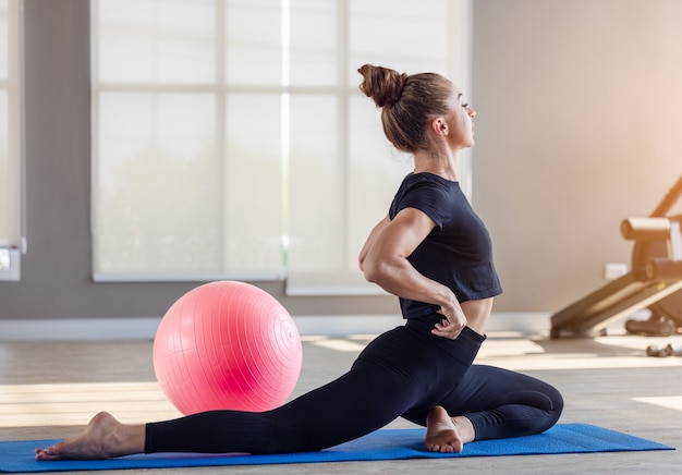 Woman in an athletic look with aerobic exercise stretching loose, Young sporty woman stretching sit in lotus pose doing yoga exercise breathing fresh air meditating in gym lit with sunlight at gym.