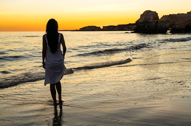 Woman at back with white dress introducing feet in the beach at sunset